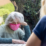 Image: Mature Woman Wearing Mask Visiting Lonely Depressed Senior Mother In Garden During Lockdown